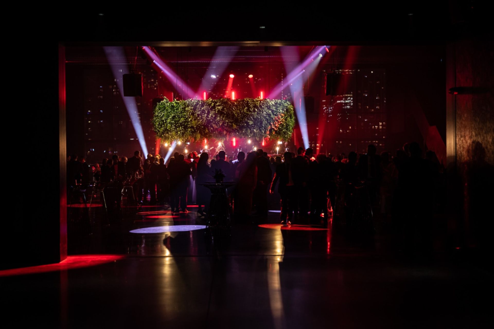 Hanging green circular foliage floral feature from event venue ceiling with event lighting illuminating the background